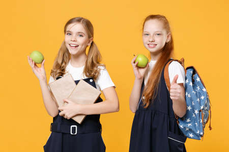 Girls 12-13 years old in white t-shirt blue school uniform dresses hold schoolbooks isolated on yellow background children studio portrait Childhood kids education lifestyle concept Mock up copy spaceの写真素材