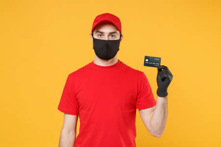 Delivery man red cap blank t-shirt uniform mask gloves isolated on yellow background studio Guy employee work courier hold credit card Service quarantine pandemic coronavirus virus 2019-ncov concept.の写真素材