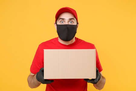 Delivery man employee in red cap blank t-shirt uniform face mask glove hold empty cardboard box isolated on yellow background studio Service quarantine pandemic coronavirus flu virus 2019-ncov conceptの写真素材