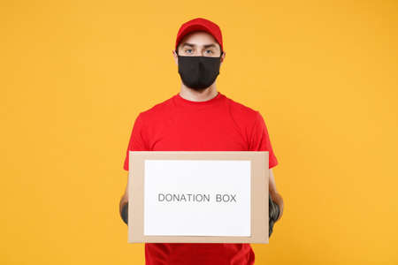 Delivery man employee in red cap blank t-shirt uniform face mask glove hold donations cardboard box isolated on yellow background studio Service quarantine pandemic coronavirus virus 2019-ncov conceptの写真素材