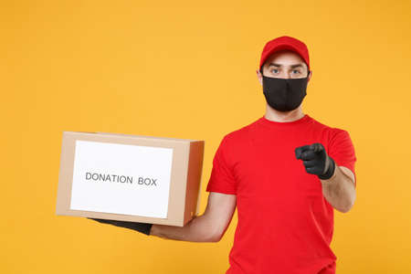 Delivery man employee in red cap blank t-shirt uniform face mask glove hold donations cardboard box isolated on yellow background studio Service quarantine pandemic coronavirus virus 2019-ncov conceptの写真素材