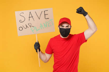 Delivery man in red cap t-shirt uniform face mask gloves hold broadsheet placard isolated on yellow background studio Guy employee working courier Service pandemic coronavirus virus 2019-ncov concept.の写真素材