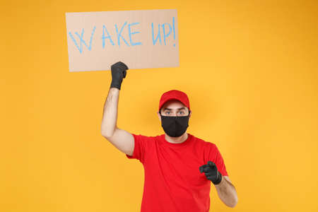 Delivery man in red cap t-shirt uniform face mask gloves hold broadsheet placard isolated on yellow background studio Guy employee working courier Service pandemic coronavirus virus 2019-ncov concept.の写真素材
