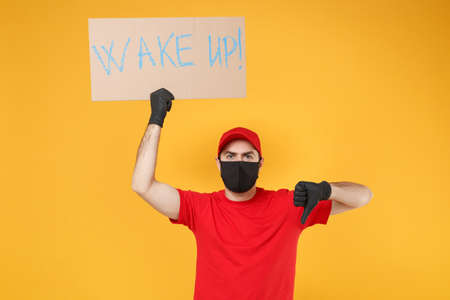 Delivery man in red cap t-shirt uniform face mask gloves hold broadsheet placard isolated on yellow background studio Guy employee working courier Service pandemic coronavirus virus 2019-ncov concept.の写真素材