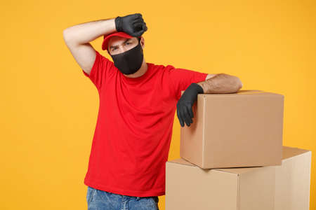 Delivery man employee in red cap blank t-shirt uniform face mask glove hold empty cardboard box isolated on yellow background studio Service quarantine pandemic coronavirus flu virus 2019-ncov conceptの写真素材