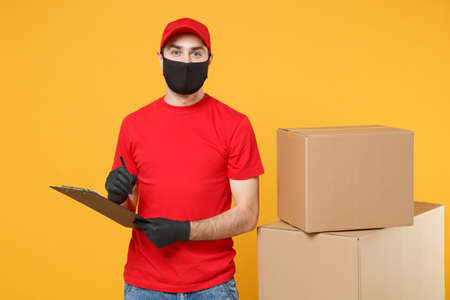 Delivery man employee in red cap blank t-shirt uniform face mask glove hold empty cardboard box isolated on yellow background studio Service quarantine pandemic coronavirus flu virus 2019-ncov conceptの写真素材