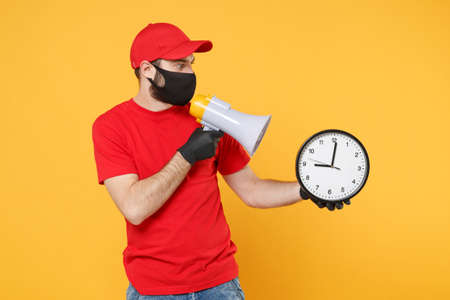 Delivery man in red cap blank t-shirt uniform mask gloves isolated on yellow background studio Guy fun employee working courier scream in megaphone Service pandemic coronavirus virus 2019-ncov conceptの写真素材