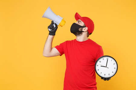 Delivery man in red cap blank t-shirt uniform mask gloves isolated on yellow background studio Guy fun employee working courier scream in megaphone Service pandemic coronavirus virus 2019-ncov conceptの写真素材
