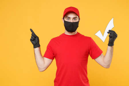 Delivery man in red cap blank t-shirt uniform sterile face mask gloves isolated on yellow background studio Guy employee working courier Service quarantine pandemic coronavirus virus 2019-ncov conceptの写真素材