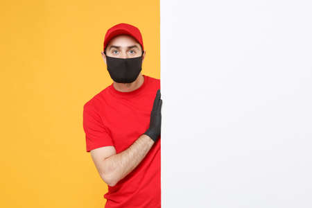 Delivery man in red cap t-shirt uniform sterile face mask gloves hold blank sign board isolated on yellow background studio Guy employee Service quarantine pandemic coronavirus virus 2019-ncov conceptの写真素材