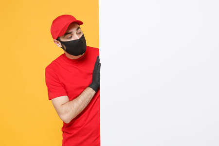Delivery man in red cap t-shirt uniform sterile face mask gloves hold blank sign board isolated on yellow background studio Guy employee Service quarantine pandemic coronavirus virus 2019-ncov conceptの写真素材