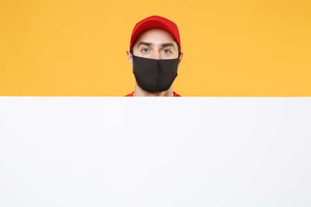 Delivery man in red cap t-shirt uniform sterile face mask gloves hold blank sign board isolated on yellow background studio Guy employee Service quarantine pandemic coronavirus virus 2019-ncov conceptの写真素材