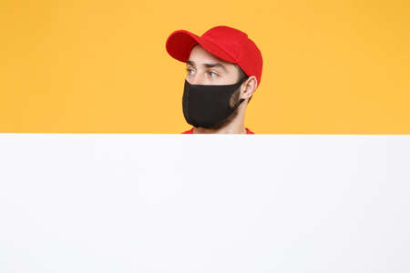 Delivery man in red cap t-shirt uniform sterile face mask gloves hold blank sign board isolated on yellow background studio Guy employee Service quarantine pandemic coronavirus virus 2019-ncov conceptの写真素材