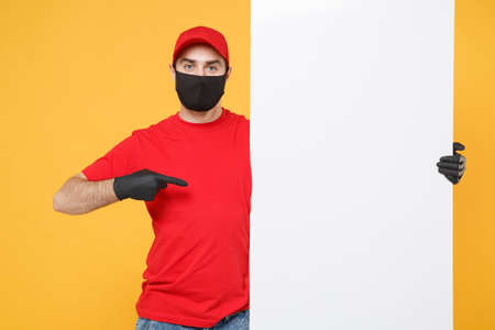 Delivery man in red cap t-shirt uniform sterile face mask gloves hold blank sign board isolated on yellow background studio Guy employee Service quarantine pandemic coronavirus virus 2019-ncov conceptの写真素材