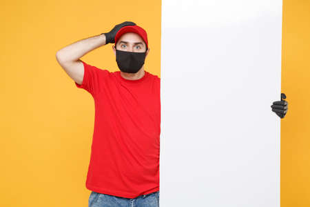 Delivery man in red cap t-shirt uniform sterile face mask gloves hold blank sign board isolated on yellow background studio Guy employee Service quarantine pandemic coronavirus virus 2019-ncov conceptの写真素材