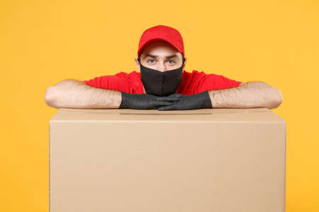 Delivery man employee in red cap blank t-shirt uniform face mask glove hold empty cardboard box isolated on yellow background studio Service quarantine pandemic coronavirus flu virus 2019-ncov conceptの写真素材