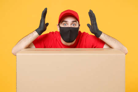 Delivery man employee in red cap blank t-shirt uniform face mask glove hold empty cardboard box isolated on yellow background studio Service quarantine pandemic coronavirus flu virus 2019-ncov conceptの写真素材