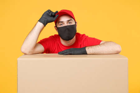Delivery man employee in red cap blank t-shirt uniform face mask glove hold empty cardboard box isolated on yellow background studio Service quarantine pandemic coronavirus flu virus 2019-ncov conceptの写真素材