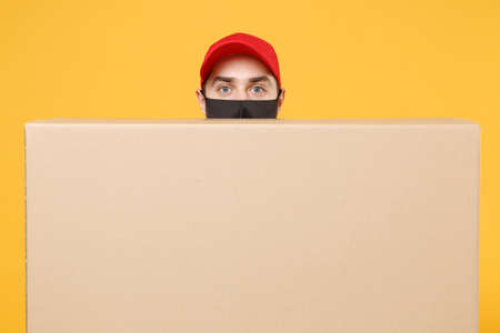 Delivery man employee in red cap blank t-shirt uniform face mask glove hold empty cardboard box isolated on yellow background studio Service quarantine pandemic coronavirus flu virus 2019-ncov conceptの写真素材