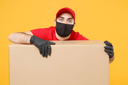 Delivery man employee in red cap blank t-shirt uniform face mask glove hold empty cardboard box isolated on yellow background studio Service quarantine pandemic coronavirus flu virus 2019-ncov conceptの写真素材