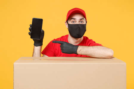 Delivery man employee in red cap blank t-shirt uniform face mask glove hold empty cardboard box isolated on yellow background studio Service quarantine pandemic coronavirus flu virus 2019-ncov conceptの写真素材