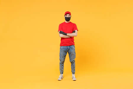 Full length delivery man in red cap t-shirt uniform sterile face mask gloves isolated on yellow background studio Guy employee courier Service quarantine pandemic coronavirus virus 2019-ncov concept.の写真素材
