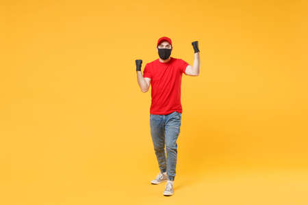 Full length delivery man in red cap t-shirt uniform sterile face mask gloves isolated on yellow background studio Guy employee courier Service quarantine pandemic coronavirus virus 2019-ncov concept.の写真素材