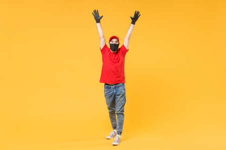 Full length delivery man in red cap t-shirt uniform sterile face mask gloves isolated on yellow background studio Guy employee courier Service quarantine pandemic coronavirus virus 2019-ncov concept.の写真素材