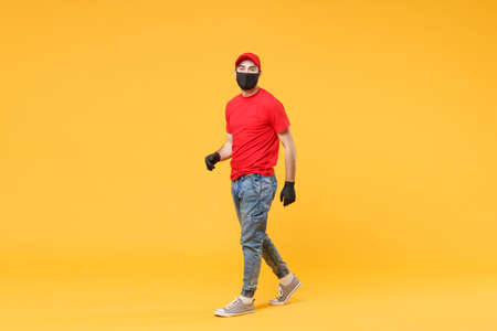 Full length delivery man in red cap t-shirt uniform sterile face mask gloves isolated on yellow background studio Guy employee courier Service quarantine pandemic coronavirus virus 2019-ncov concept.の写真素材