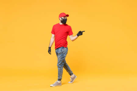 Full length delivery man in red cap t-shirt uniform sterile face mask gloves isolated on yellow background studio Guy employee courier Service quarantine pandemic coronavirus virus 2019-ncov concept.の写真素材