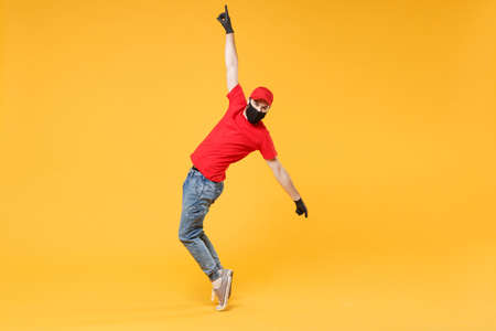 Full length delivery man in red cap t-shirt uniform sterile face mask gloves isolated on yellow background studio Guy employee courier Service quarantine pandemic coronavirus virus 2019-ncov concept.の写真素材
