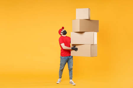 Delivery man employee in red cap blank t-shirt uniform face mask glove hold empty cardboard box isolated on yellow background studio Service quarantine pandemic coronavirus flu virus 2019-ncov conceptの写真素材