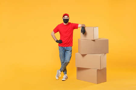 Delivery man employee in red cap blank t-shirt uniform face mask glove hold empty cardboard box isolated on yellow background studio Service quarantine pandemic coronavirus flu virus 2019-ncov conceptの写真素材