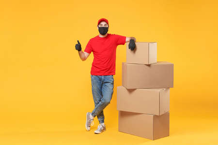 Delivery man employee in red cap blank t-shirt uniform face mask glove hold empty cardboard box isolated on yellow background studio Service quarantine pandemic coronavirus flu virus 2019-ncov conceptの写真素材