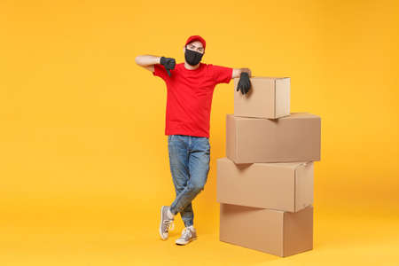 Delivery man employee in red cap blank t-shirt uniform face mask glove hold empty cardboard box isolated on yellow background studio Service quarantine pandemic coronavirus flu virus 2019-ncov conceptの写真素材