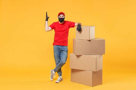 Delivery man employee in red cap blank t-shirt uniform face mask glove hold empty cardboard box isolated on yellow background studio Service quarantine pandemic coronavirus flu virus 2019-ncov conceptの写真素材