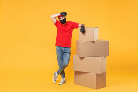 Delivery man employee in red cap blank t-shirt uniform face mask glove hold empty cardboard box isolated on yellow background studio Service quarantine pandemic coronavirus flu virus 2019-ncov conceptの写真素材