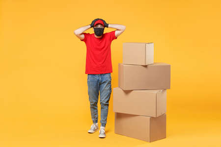 Delivery man employee in red cap blank t-shirt uniform face mask glove hold empty cardboard box isolated on yellow background studio Service quarantine pandemic coronavirus flu virus 2019-ncov conceptの写真素材