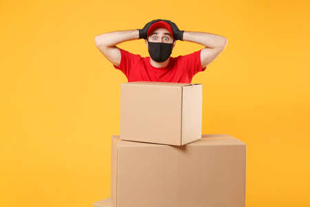 Delivery man employee in red cap blank t-shirt uniform face mask glove hold empty cardboard box isolated on yellow background studio Service quarantine pandemic coronavirus flu virus 2019-ncov conceptの写真素材