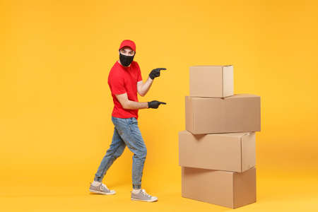 Delivery man employee in red cap blank t-shirt uniform face mask glove hold empty cardboard box isolated on yellow background studio Service quarantine pandemic coronavirus flu virus 2019-ncov conceptの写真素材
