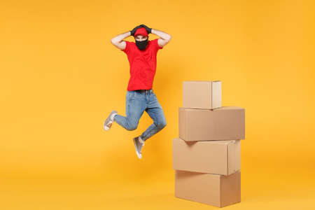 Delivery man employee in red cap blank t-shirt uniform face mask glove hold empty cardboard box isolated on yellow background studio Service quarantine pandemic coronavirus flu virus 2019-ncov conceptの写真素材