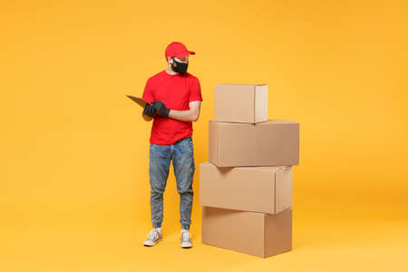 Delivery man employee in red cap blank t-shirt uniform face mask glove hold empty cardboard box isolated on yellow background studio Service quarantine pandemic coronavirus flu virus 2019-ncov conceptの写真素材