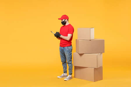 Delivery man employee in red cap blank t-shirt uniform face mask glove hold empty cardboard box isolated on yellow background studio Service quarantine pandemic coronavirus flu virus 2019-ncov conceptの写真素材
