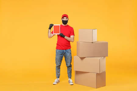 Delivery man employee in red cap blank t-shirt uniform face mask glove hold empty cardboard box isolated on yellow background studio Service quarantine pandemic coronavirus flu virus 2019-ncov conceptの写真素材