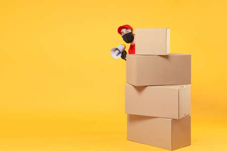 Delivery man employee in red cap blank t-shirt uniform face mask glove hold empty cardboard box isolated on yellow background studio Service quarantine pandemic coronavirus flu virus 2019-ncov conceptの写真素材