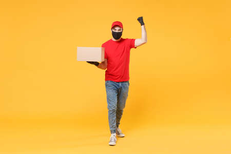 Delivery man employee in red cap blank t-shirt uniform face mask glove hold empty cardboard box isolated on yellow background studio Service quarantine pandemic coronavirus flu virus 2019-ncov conceptの写真素材