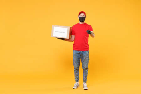 Delivery man employee in red cap blank t-shirt uniform face mask glove hold donations cardboard box isolated on yellow background studio Service quarantine pandemic coronavirus virus 2019-ncov conceptの写真素材