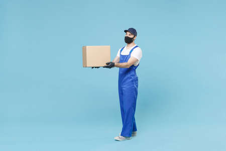 Full length delivery man in cap t-shirt uniform sterile face mask gloves isolated on blue background...