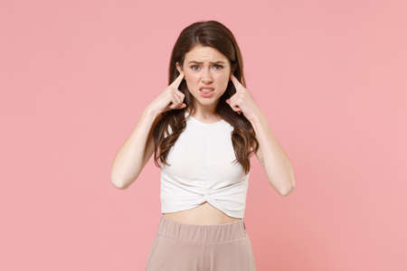 Displeased young brunette woman girl in light casual clothes posing isolated on pastel pink wall background studio portrait. People lifestyle concept. Mock up copy space. Covering ears with fingers.の写真素材