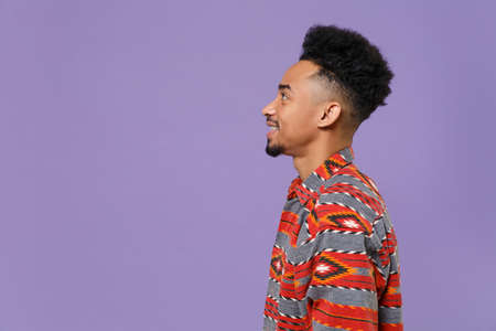 Side view of smiling young african american guy in casual colorful shirt posing isolated on violet background studio portrait. People emotions lifestyle concept. Mock up copy space. Looking aside.の写真素材